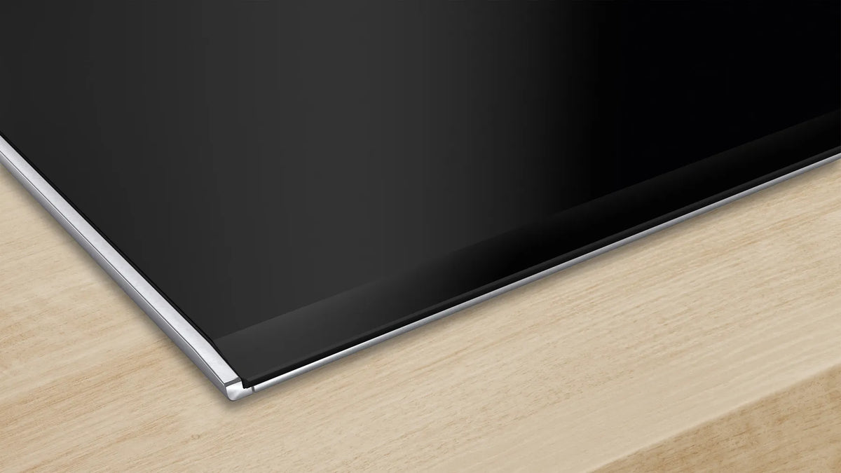 Close-up of Bosch PIB375FB5I black ceramic-glass corner with metal edge on a wooden counter