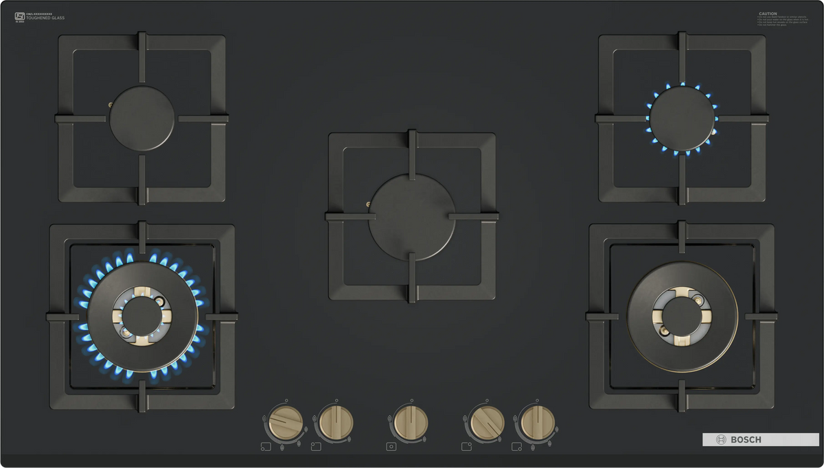 Top view of Bosch PNV9B6G21I gas hob showing five burners, pan supports and brass-finish knobs with lit flames