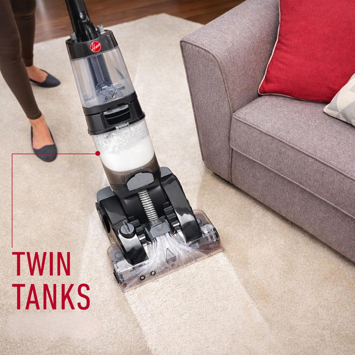 Hoover CWKTH012 Platinum Power Max washing a carpet beside a sofa, with the twin tanks highlighted