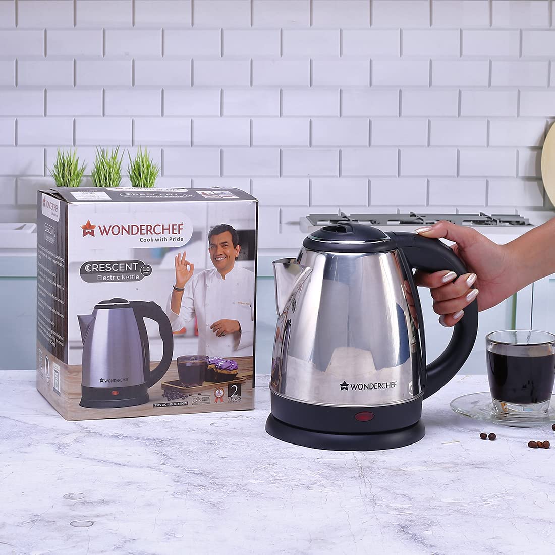 Wonderchef Crescent 1.8 L electric kettle held by the handle beside its retail box on a marble counter