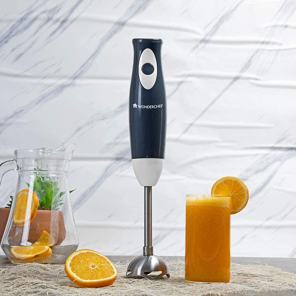 Wonderchef Ultima Plus hand blender on a counter with a glass of orange juice, orange slices and a jug