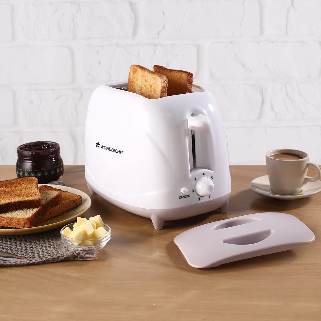 Wonderchef Ultima toaster with two toasted slices popping up, beside a plate of toast, butter, jam, coffee and the removed lid cover