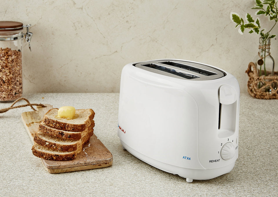 Bajaj ATX 4 white toaster on a worktop beside buttered multigrain bread slices on a wooden board