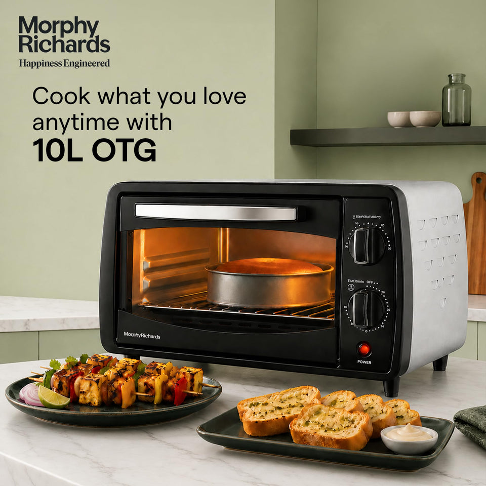 Morphy Richards 510065 10 L OTG oven on a kitchen counter with a cake baking inside, beside paneer skewers and garlic bread