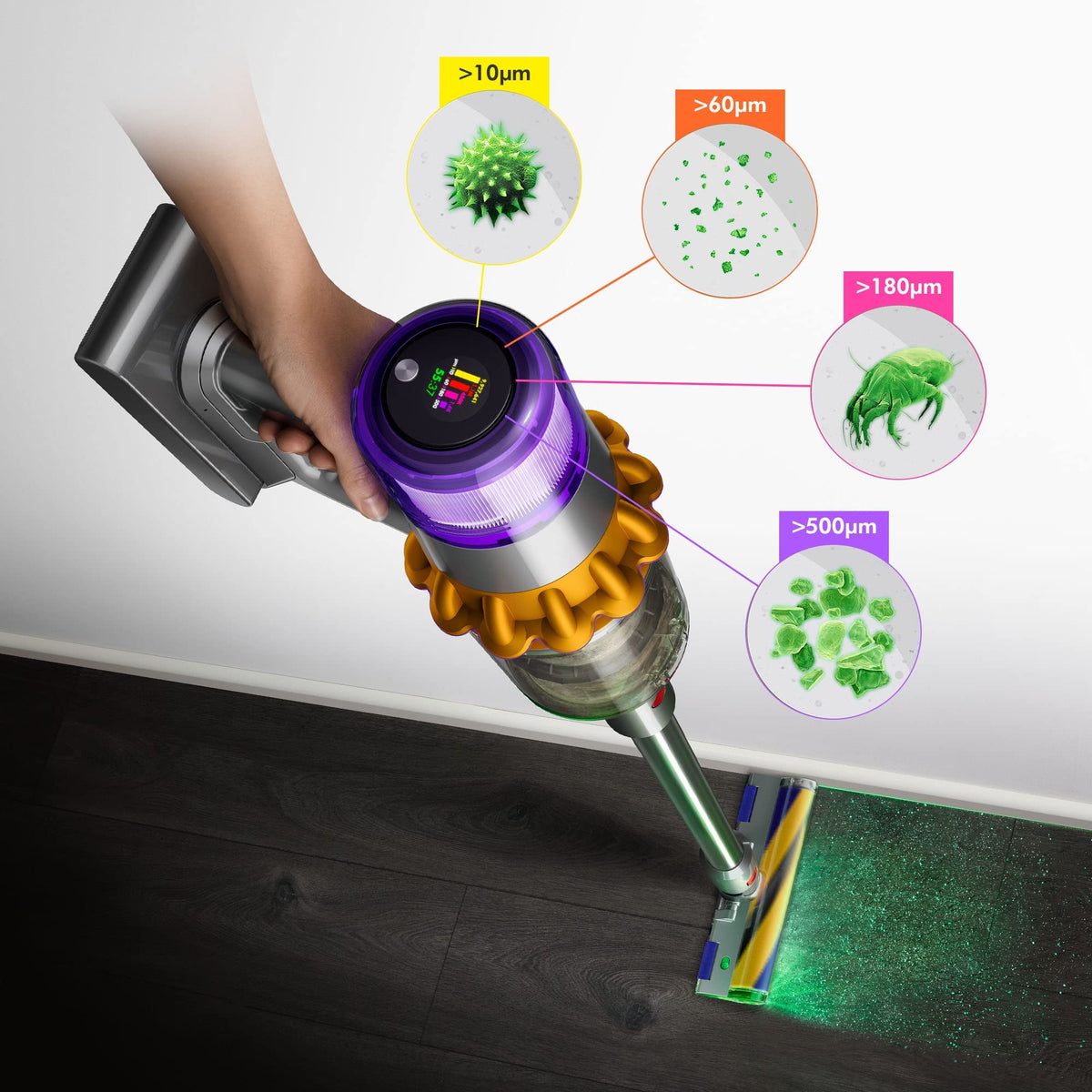 Dyson V15 Detect 381356-01 held in hand showing the LCD screen and dust particle size callouts while the cleaner head lights up a dark wood floor