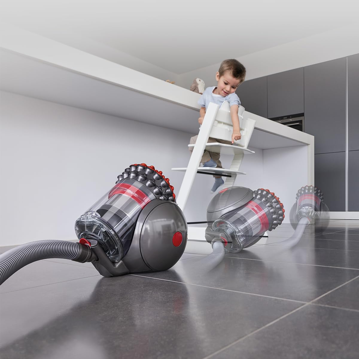 Dyson Big Ball 492954-01 vacuum moving across a tiled kitchen floor while a child watches from a high chair
