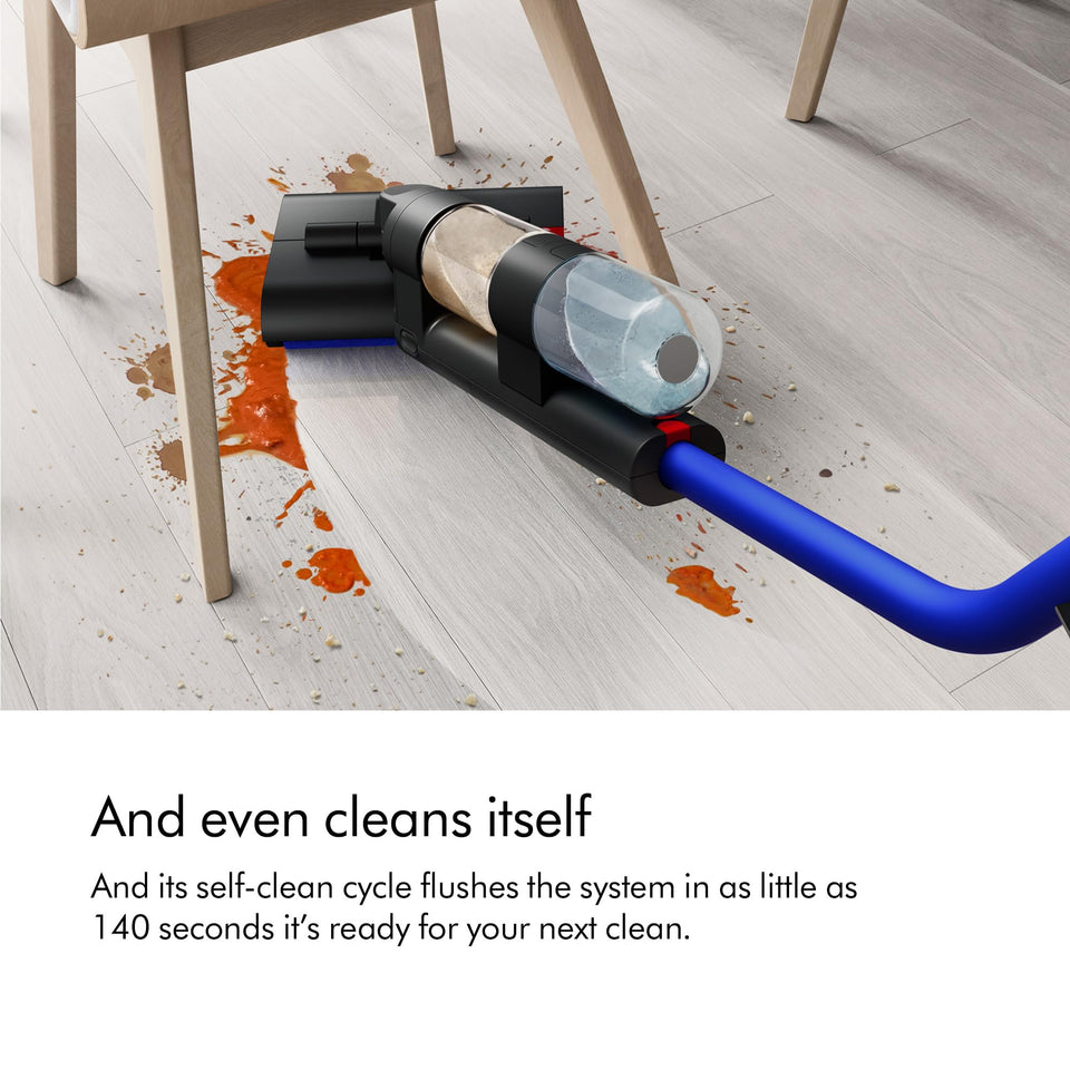 Dyson WashG1 492608-01 reaching low under a chair to clean a sauce spill on a wooden floor