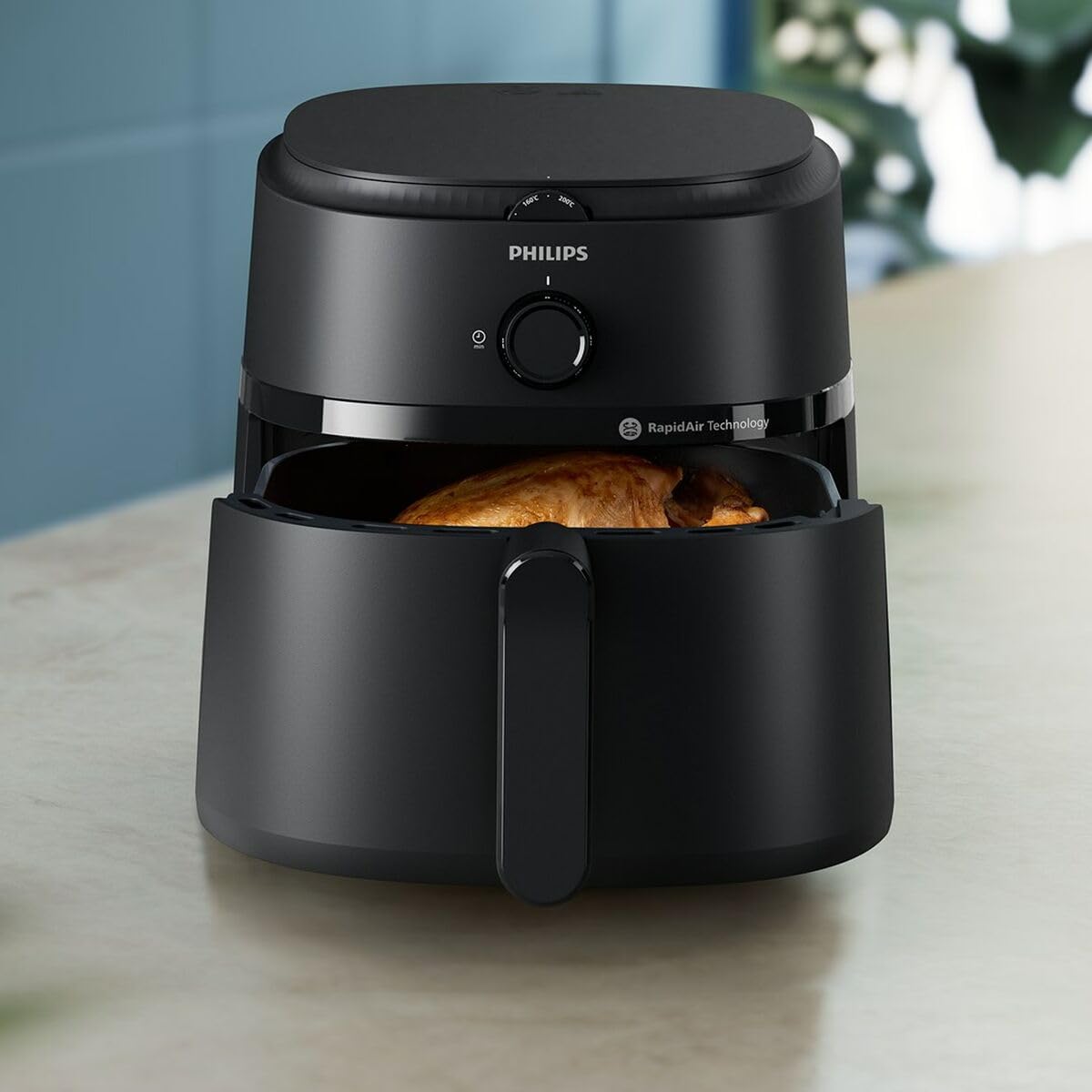 Philips NA130/00 air fryer on a kitchen counter with the basket partly open showing a roast chicken