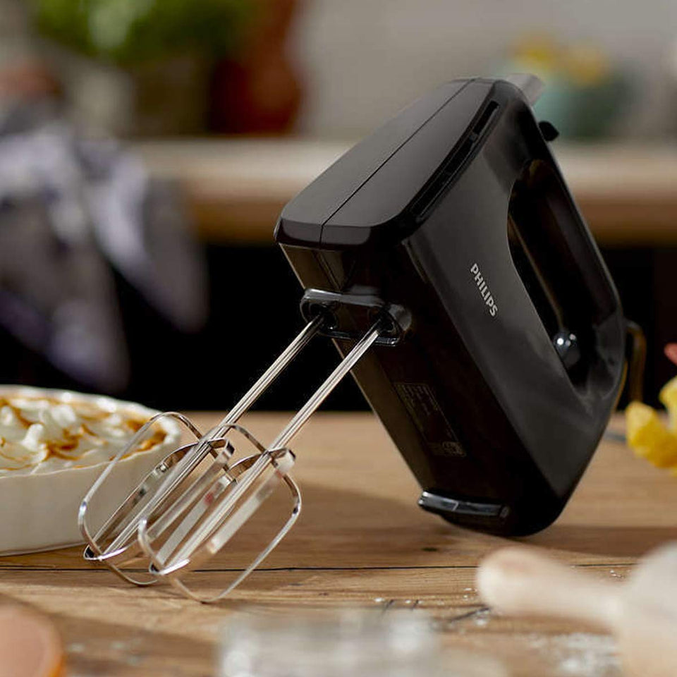 Philips HR3705/10 black hand mixer resting on a wooden counter with beaters pointing down beside a baked dessert